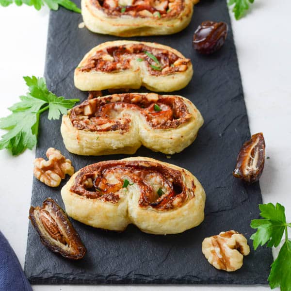 Prosciutto and Date Palmiers on a platter with dates and walnuts.