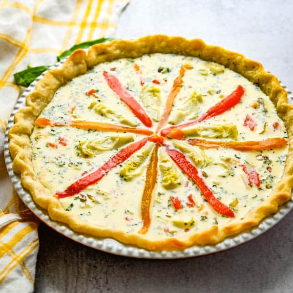garnishing vegetable quiche with roasted bell peppers and baby artichokes.