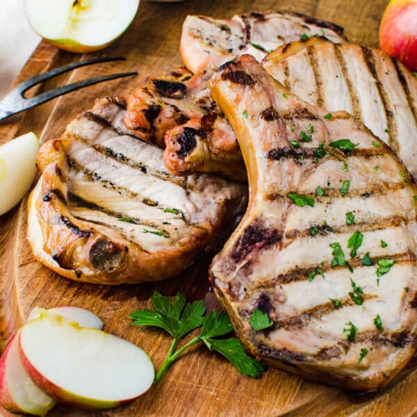 A cutting board with several brined grilled pork chops with slices of apple and fresh parsley for garnish.
