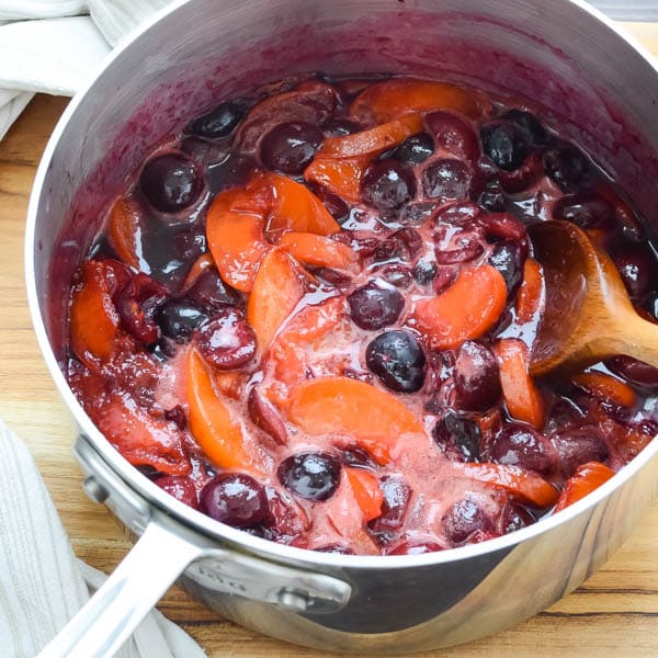 cherries and nectarines in a pot with a spoon.