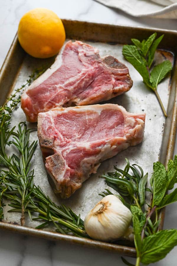 veal loin chops on a sheet pan with fresh herbs, garlic and lemon.