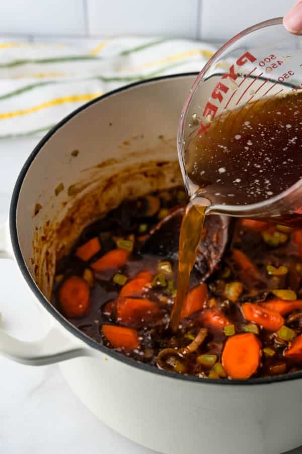 pouring beef broth into the dutch oven.