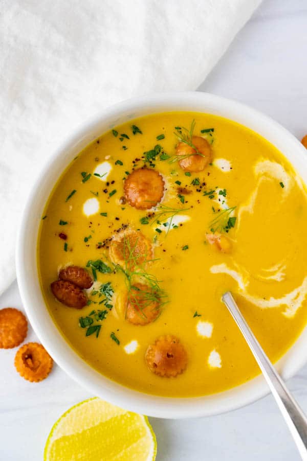 a bowl of creamy pumpkin soup with croutons, cream and lime juice.