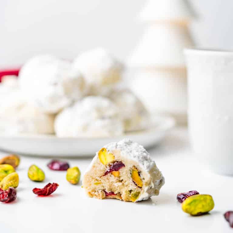 Tea cookies with cranberries and pistachios on a plate with a cup of tea.