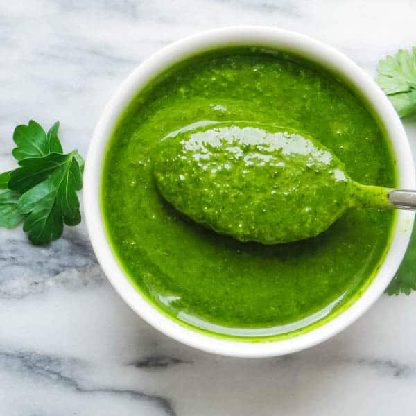 Green sauce in a bowl with a spoon dipping into it.