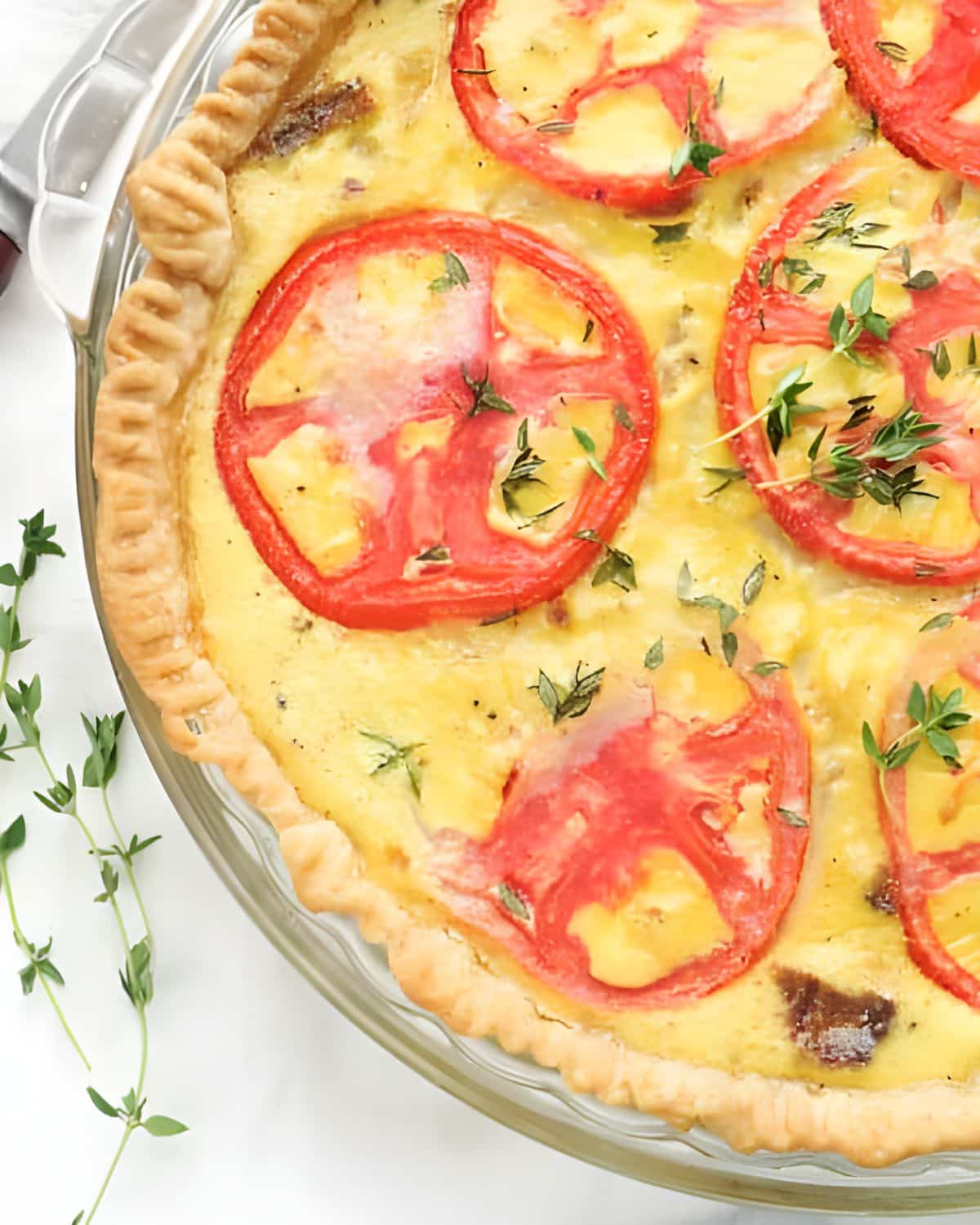 Tomato Bacon and Onion Quiche with herbs in a pie plate.