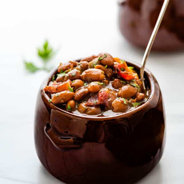 Old fashioned baked beans in a crock with a spoon.