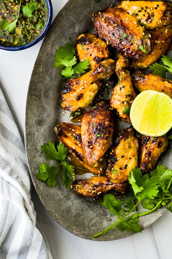chicken wings on a platter with cilantro, sesame seeds and fresh lime.