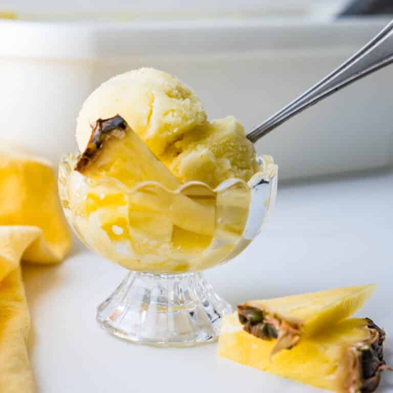 A footed glass dessert bowl filled with pineapple sorbet and slices of fresh pineapple.