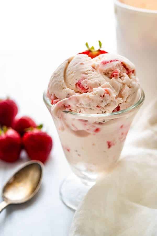 A dish of homemade strawberry ice cream with a spoon and linen napkin along with fresh berries.