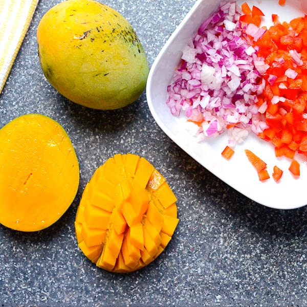 a mango cut into a diamond pattern and chopped onions and red peppers
