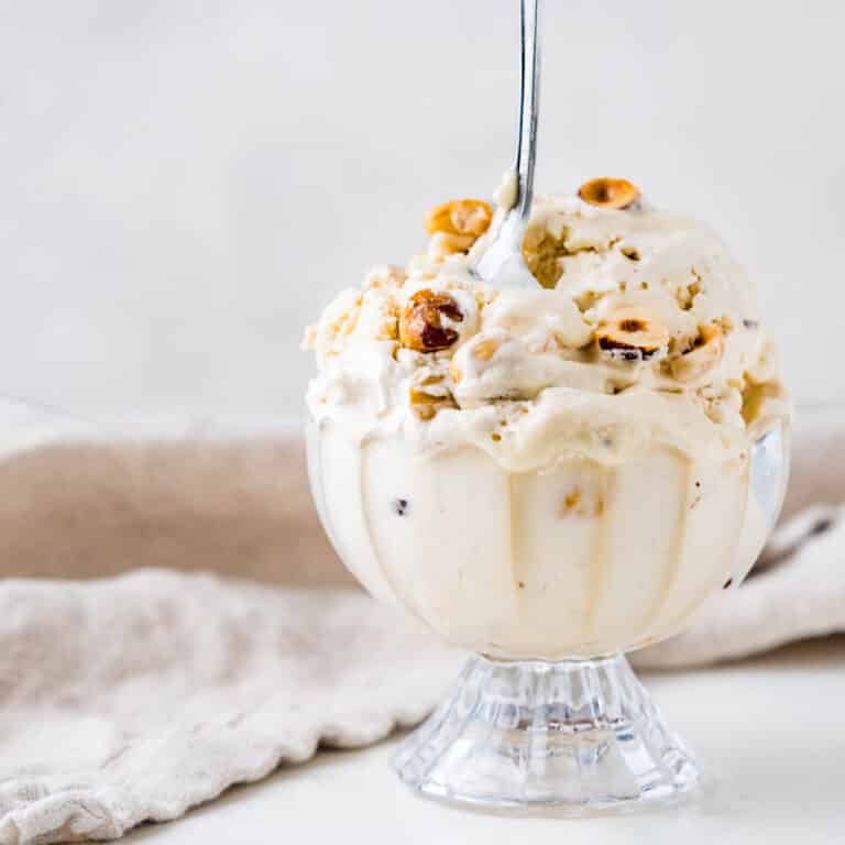 A bowl of hazelnut nougat ice cream with a spoon and chopped nuts.