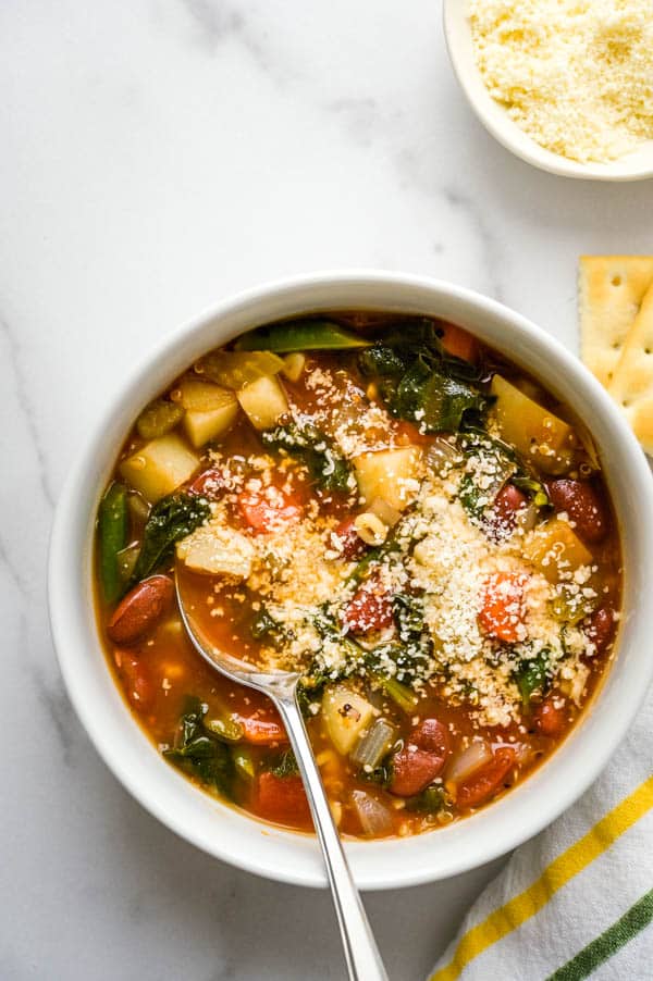an overhead shot of healthy vegetable minestrone with parmesan cheese and crackers.