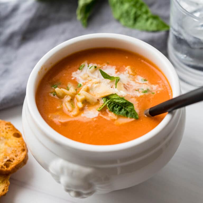creamy tomato soup in a bowl with parmesan and basil garnish.