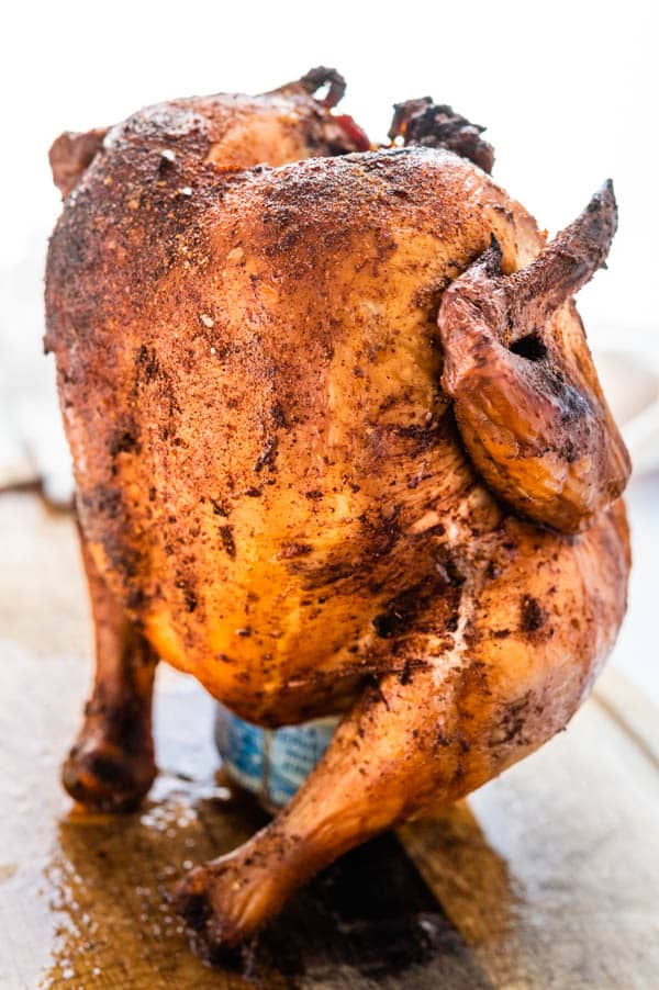 smoked beer can chicken resting upright on it's beer can stand on a cutting board
