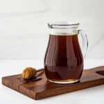 honey simple syrup in a small pitcher on a wooden board.