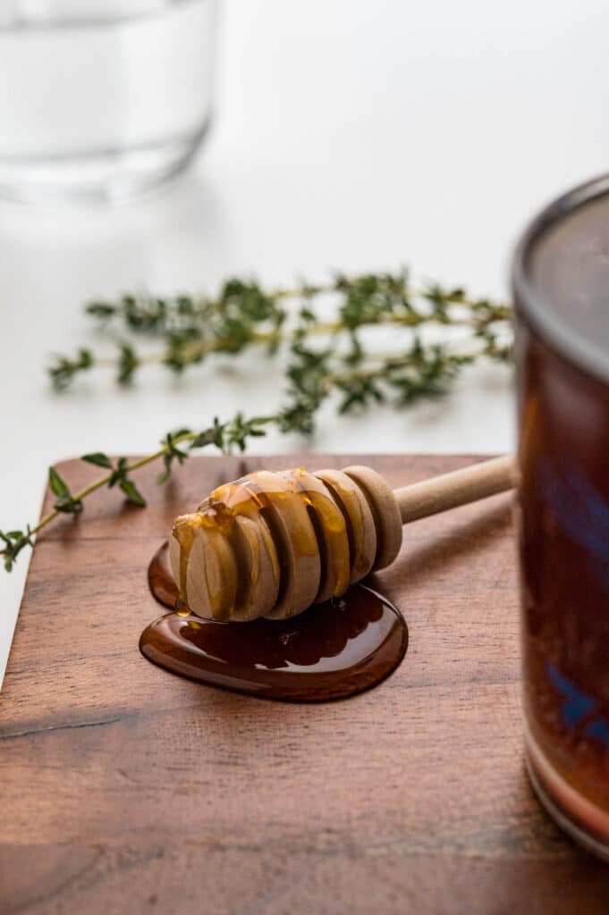 a honey dipper with honey and thyme leaves in the background.