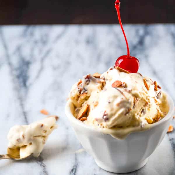 Cherry Amaretto Crunch Ice Cream in a bowl with a spoonful on a marble board.