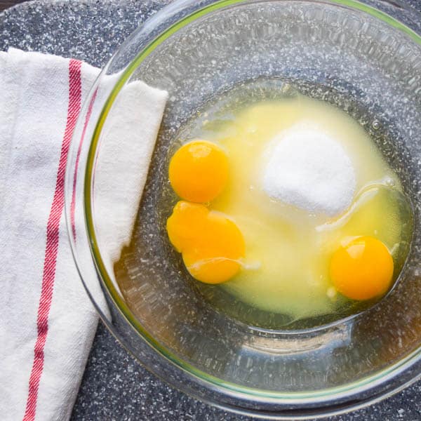 sugar and eggs in a glass bowl with a dish towel on the side.