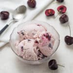 A bowl of cherry ice cream surrounded by black cherries.