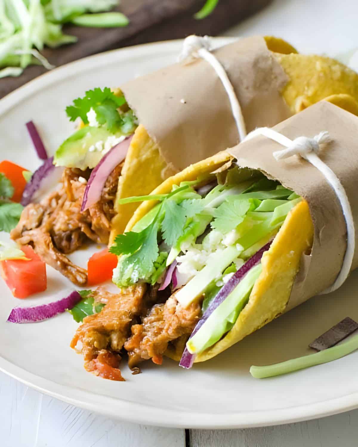 A plate of braised pork tacos with cabbage and tomatoes.