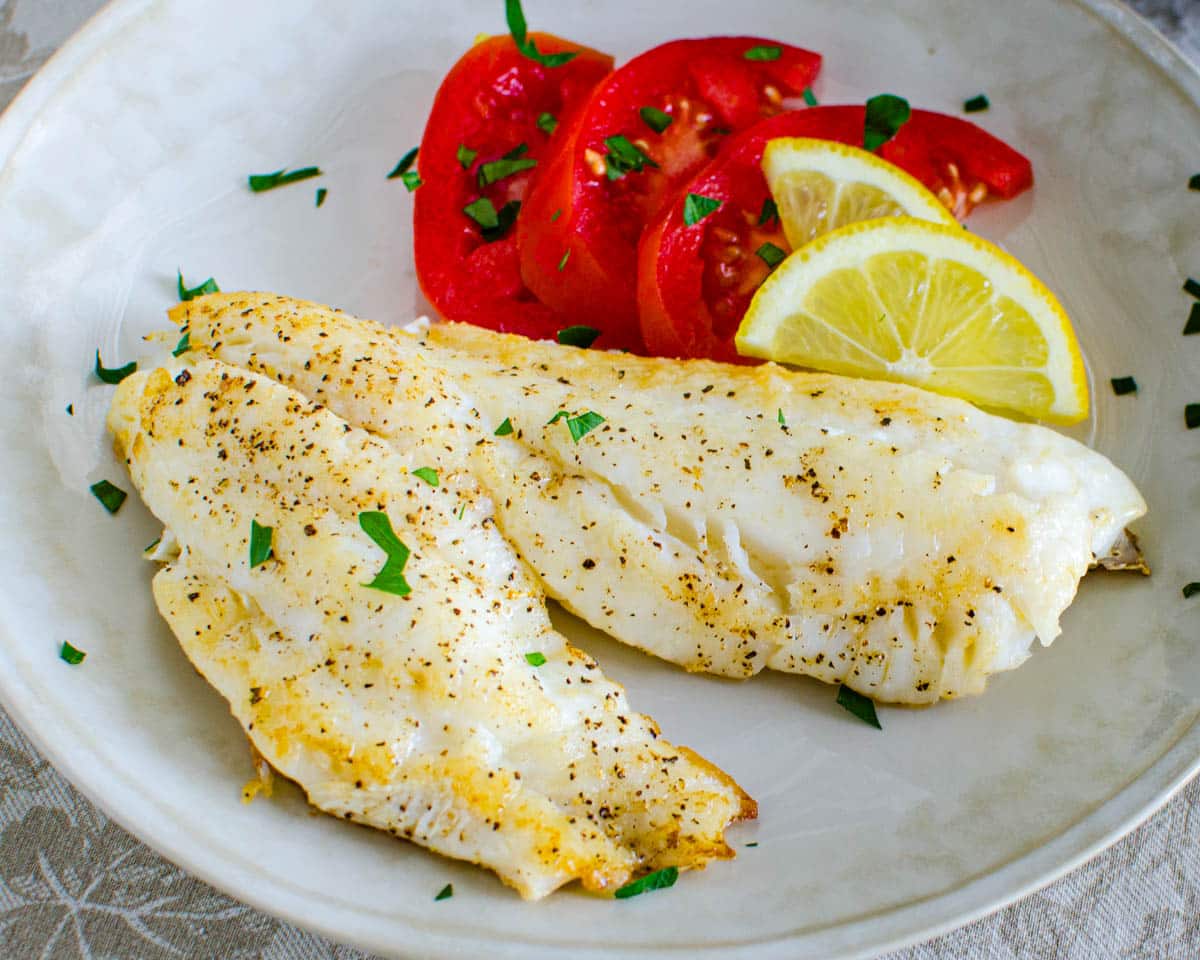 A plate of cooked hogfish snapper and tomato slices.