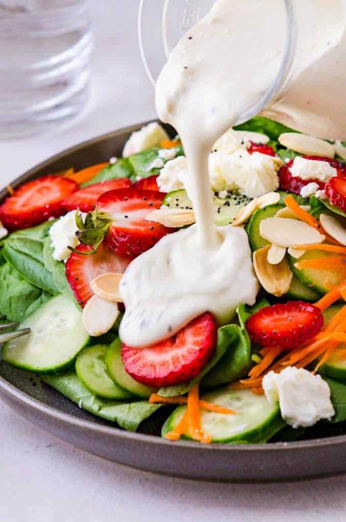 adding the creamy dressing to the spinach and strawberry salad.