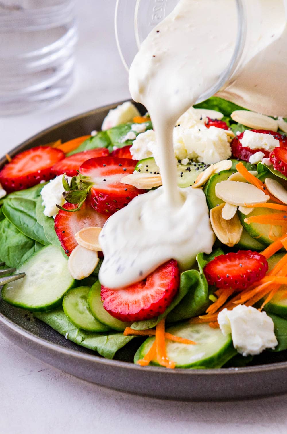 adding the creamy dressing to the spinach and strawberry salad.