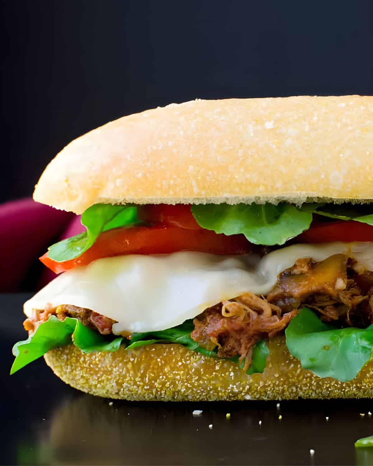 A braised pork sandwich with cheese and tomato.
