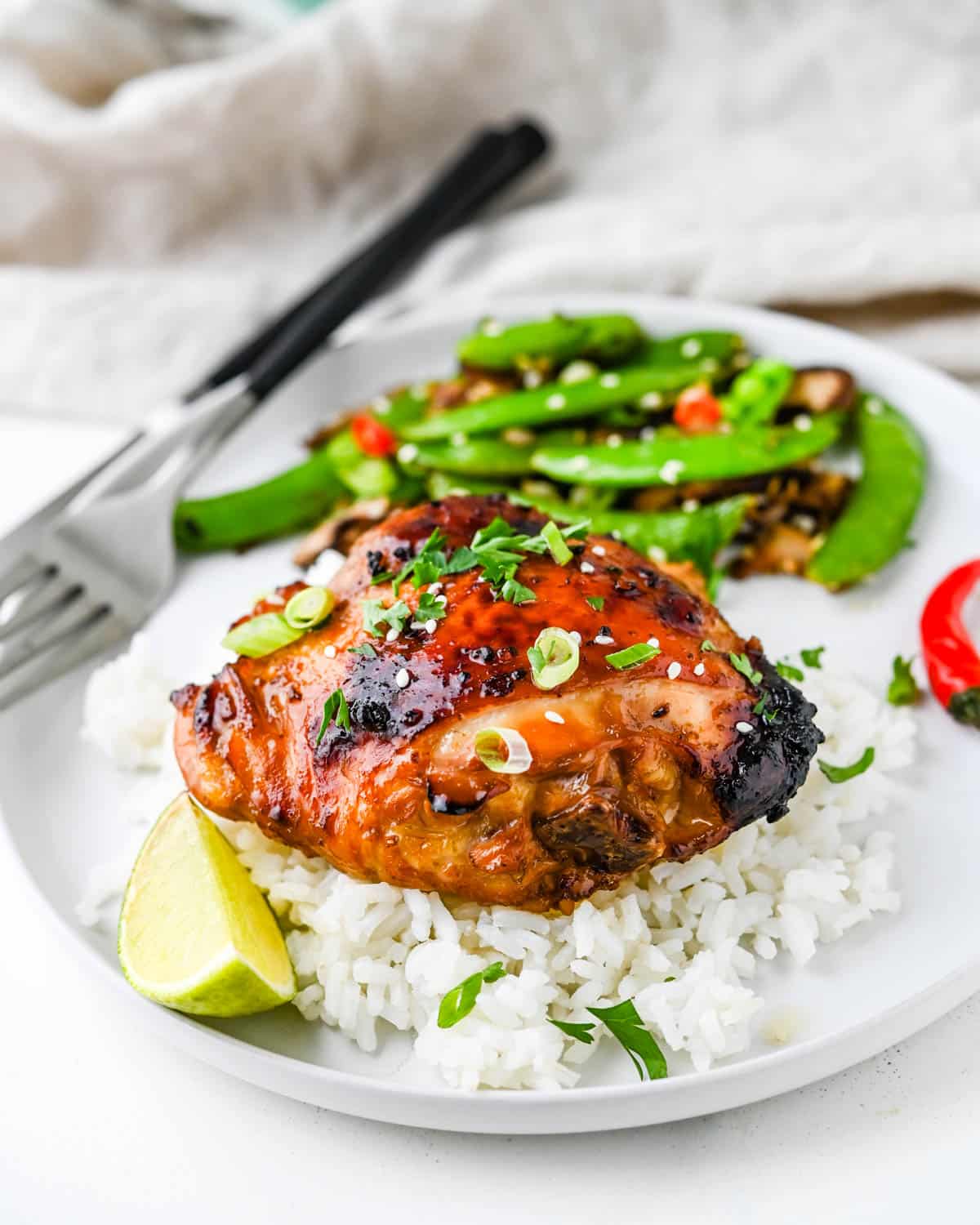 A juicy baked chicken thigh served with rice and snap peas.