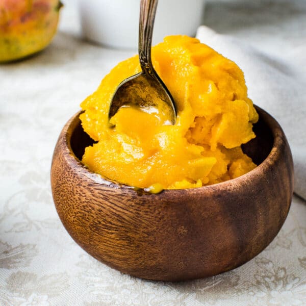 pineapple mango sorbet in a wooden bowl with a spoon.