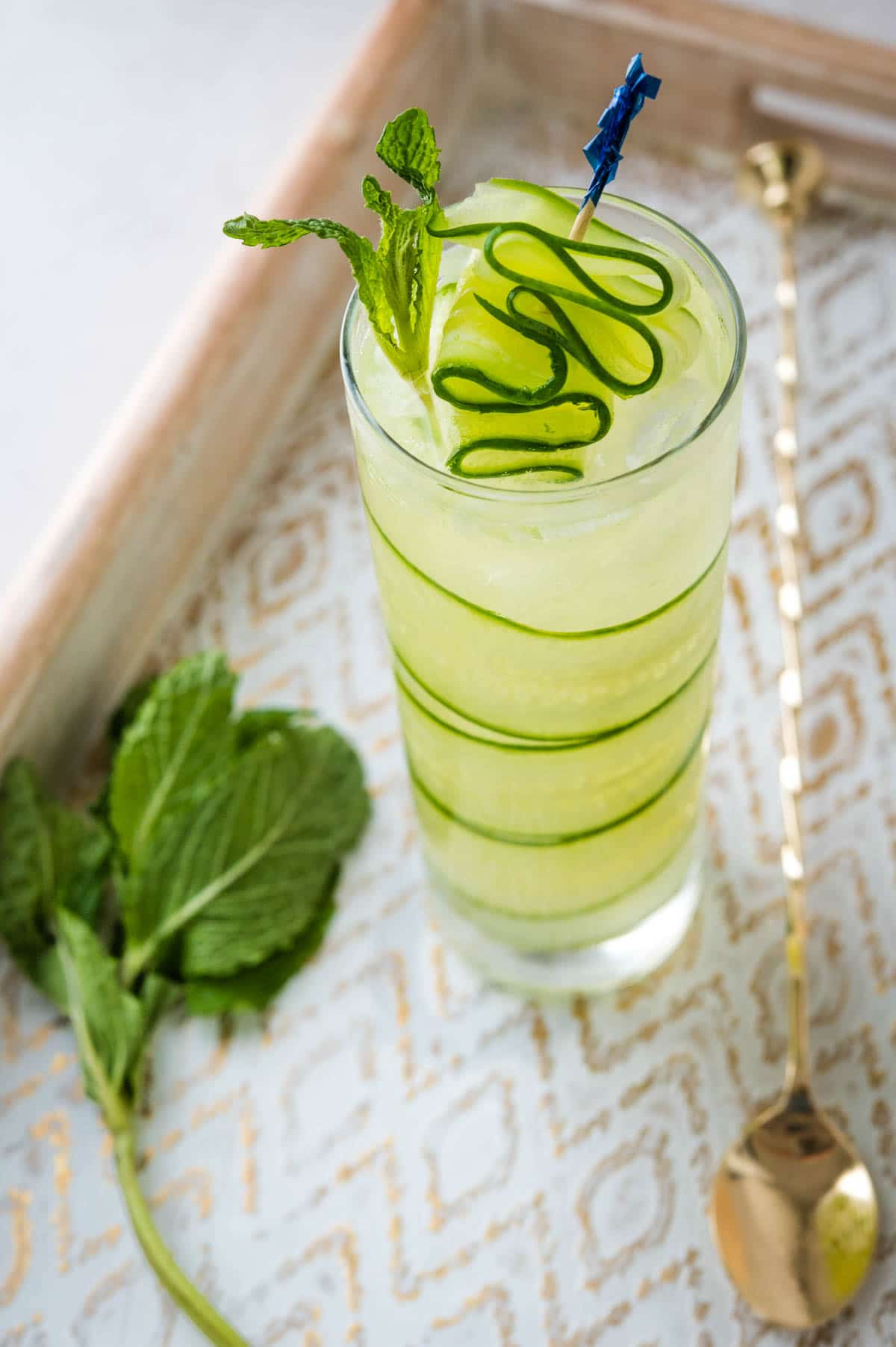 Serving a cucumber pioneer with cucumber garnish on a white and gold tray.