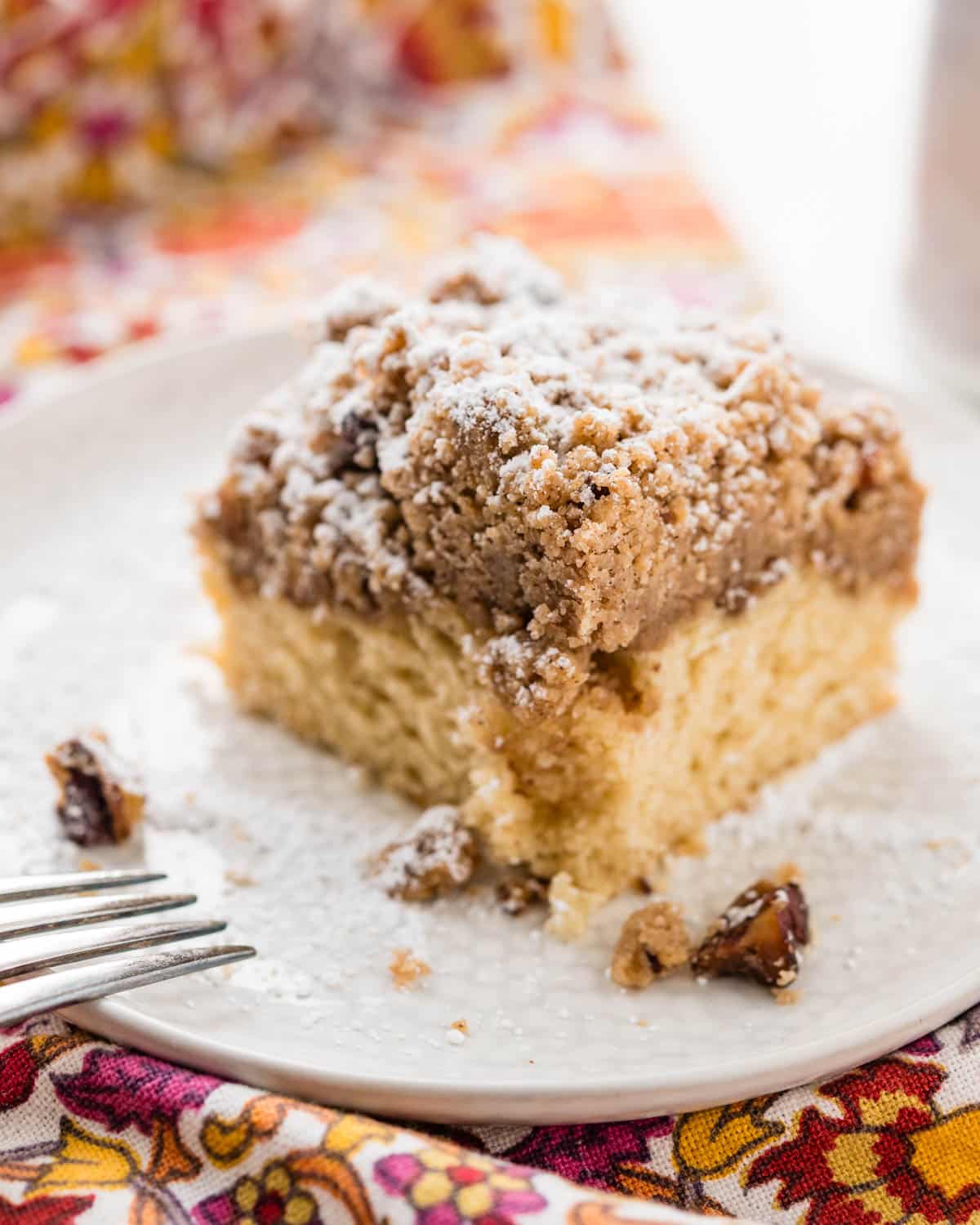 A thick slice of new york style crumb cake on a plate with powdered sugar.