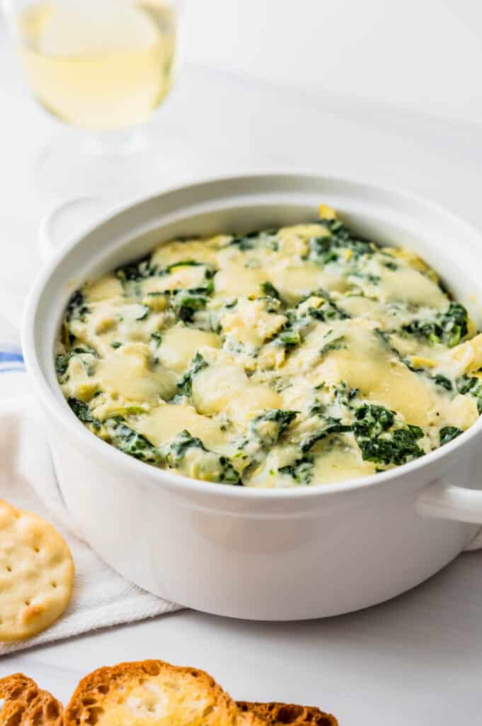 a hot dish of baked spinach artichoke dip with crackers and wine.