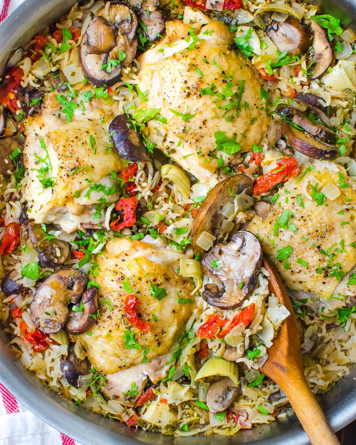Mediterranean chicken and rice in a skillet with a wooden spoon.