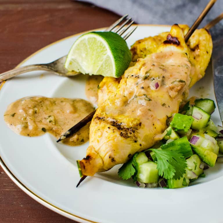 chicken satay on a skewer with peanut sauce and cucumber avocado relish on the side.