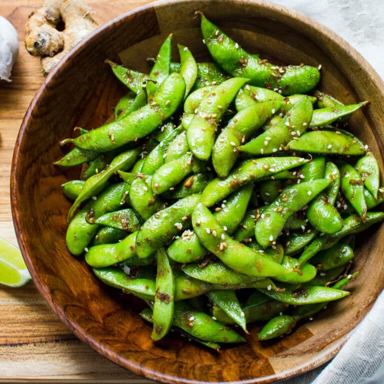 A wooden bowl of edamame with ginger and garlic.