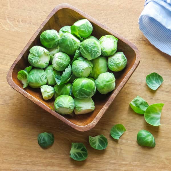 a wooden bowl filled with trimmed brussels sprouts.