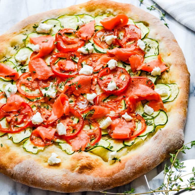 A pizza topped with thin slices of zucchini, tomato, smoked salmon and chèvre.