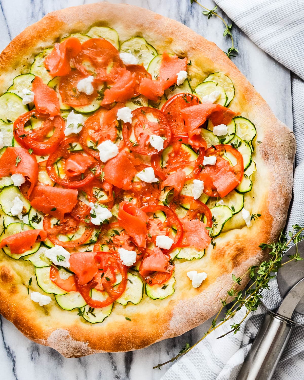 A smoked salmon pizza with thin slices of zucchini and goat cheese.