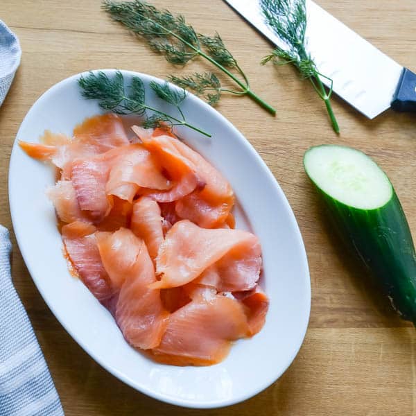 smoked salmon, cucumber and dill on a cutting board.