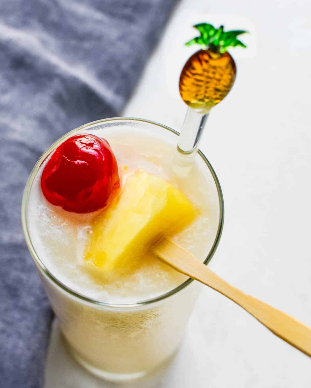 A tallboy pina colada with cherry and pineapple garnish.