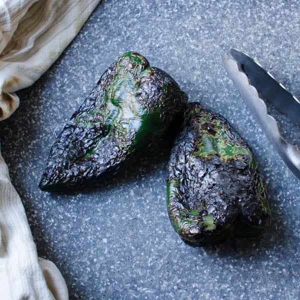 charred poblanos with tongs