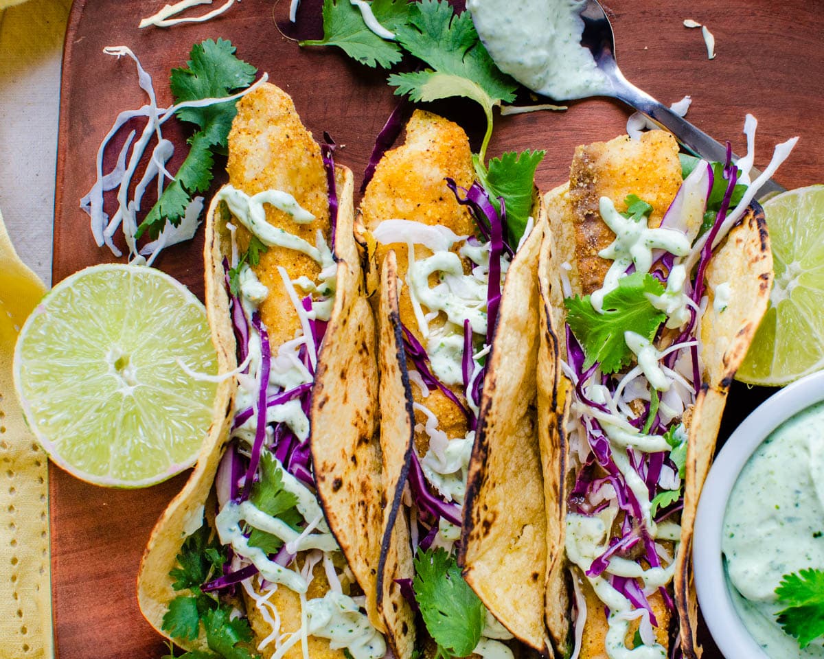 A platter of fish tacos with cabbage, lime and crema. 