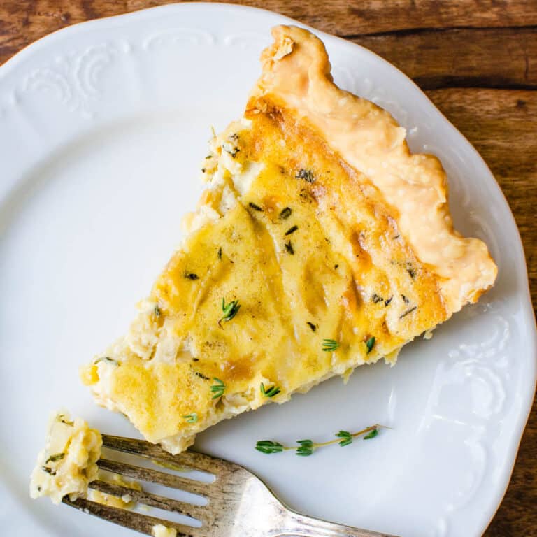 A slice of caramelized onion quiche on a plate with a fork.