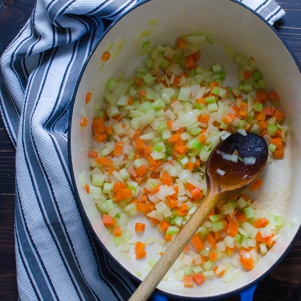 onions, carrots and celery in a dutch oven with a spoon