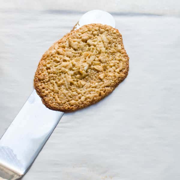 Coconut Cashew Tuiles on a cookie sheet with an offset spatula