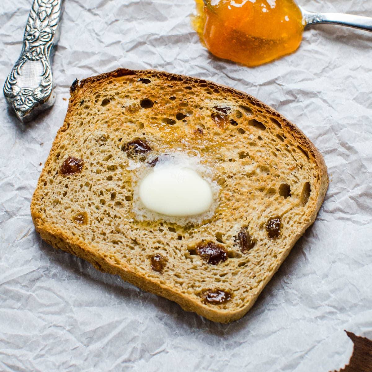 A slice of toasted oatmeal raisin bread with a spoonful of jam.
