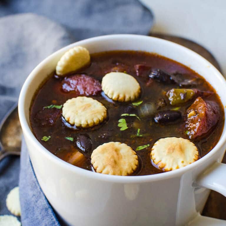 A cup of black bean sausage soup with oyster crackers.