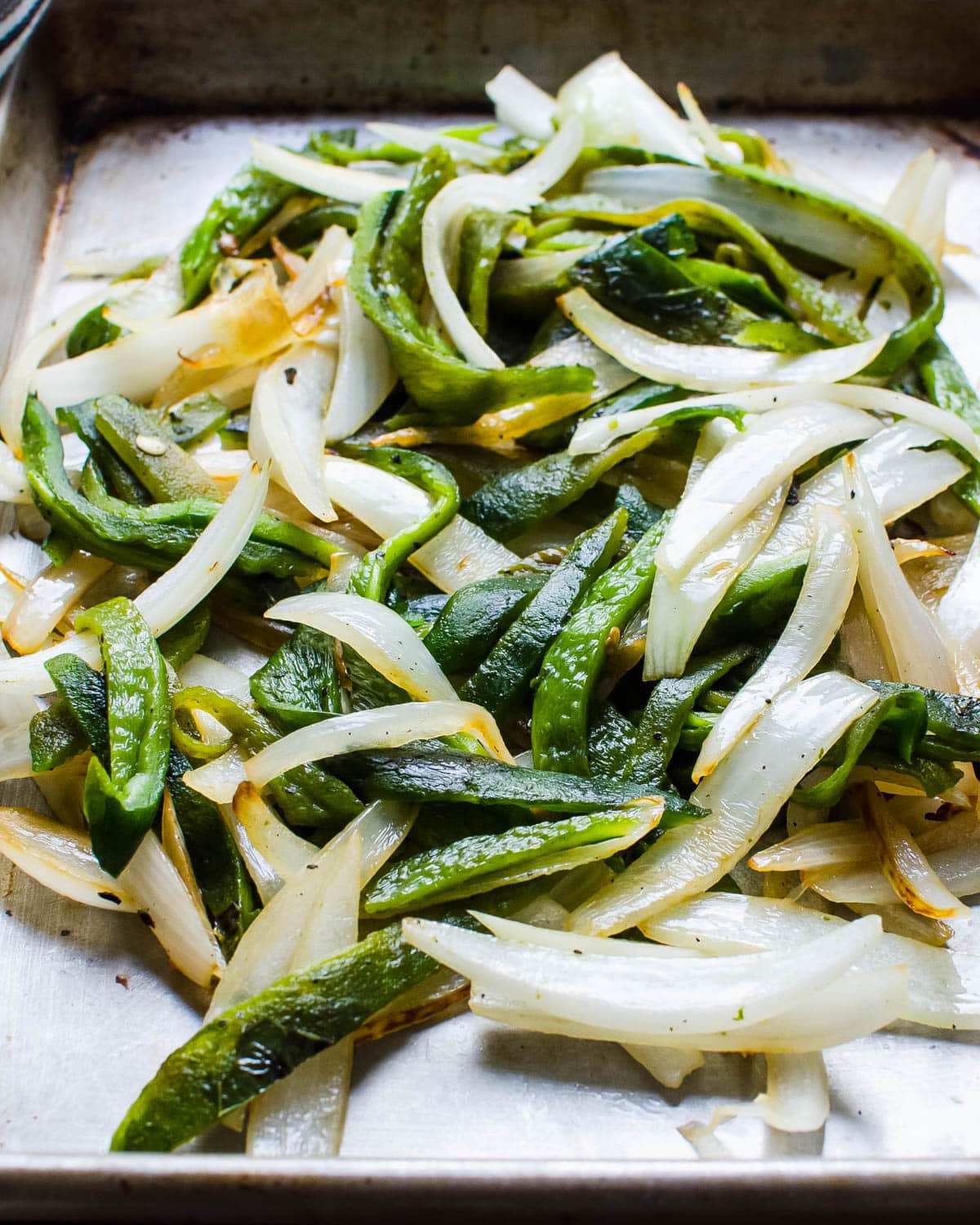 Fire roasted poblano peppers and white onions on a baking sheet.